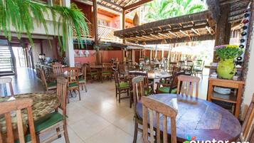Een ruim restaurant met houten tafels en stoelen, een rieten dak en hangende varens.