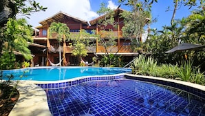 A pool area with a tiled floor, surrounded by lush greenery and a multi-story building with balconies. - Pousada Casa Do Forte (Mata de São João)