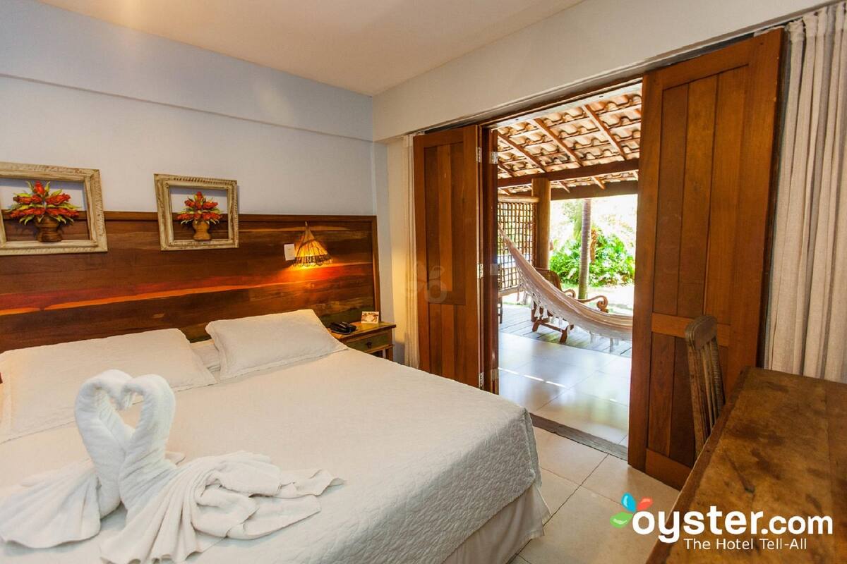 A hotel room with a bed, two framed pictures, a nightstand, and a view of a hammock outside.