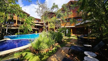 Una piscina rodeada de abundante vegetación y un patio con mobiliario exterior.