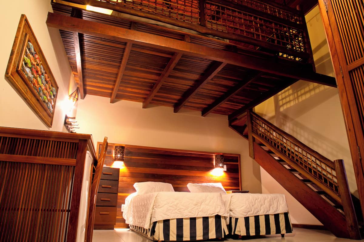 A bedroom with a wooden headboard, a bed with white bedding, a nightstand, and a staircase with a wooden railing.