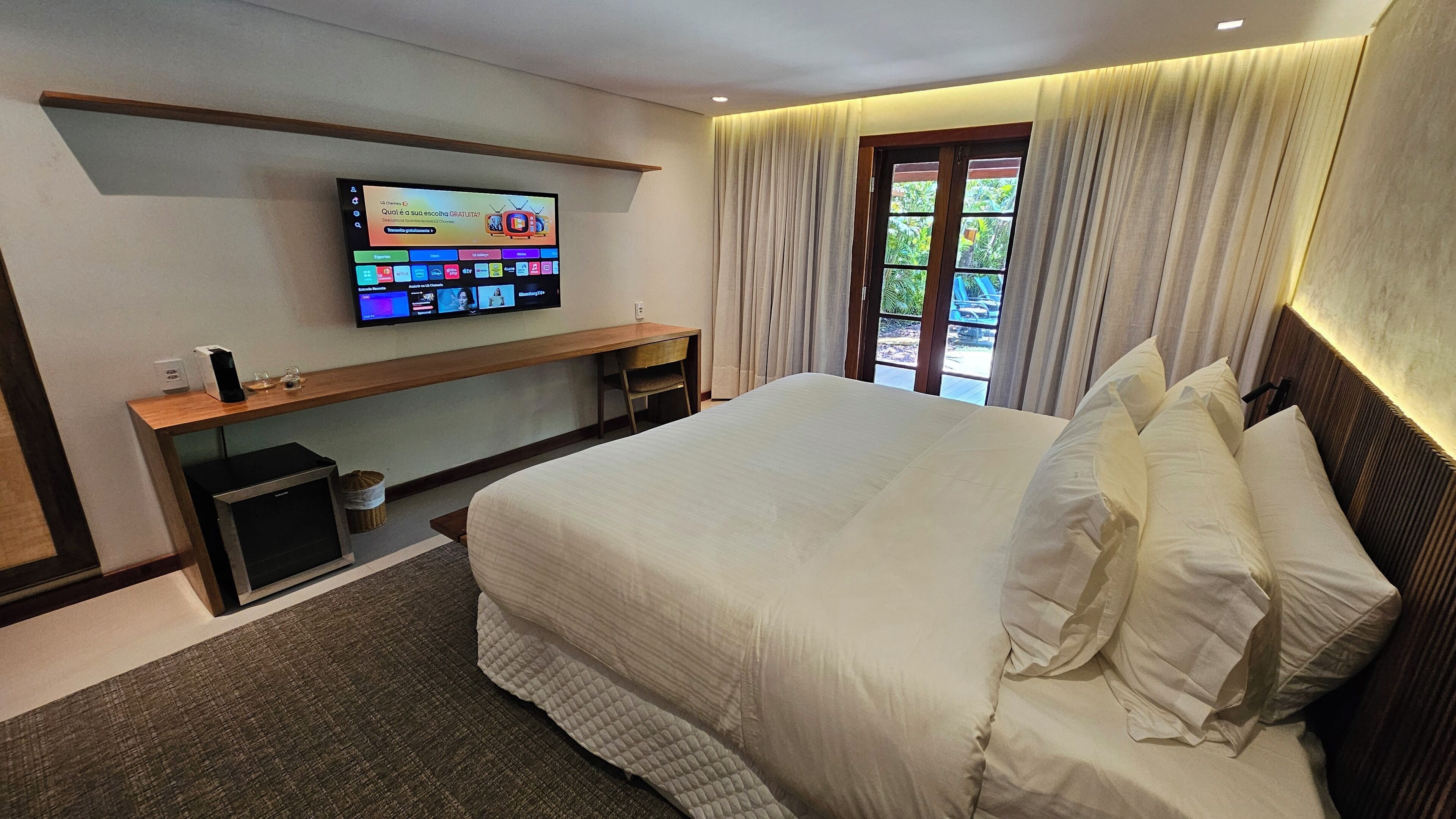 A hotel room with a large bed, a TV mounted on the wall, a desk, and a window with curtains.