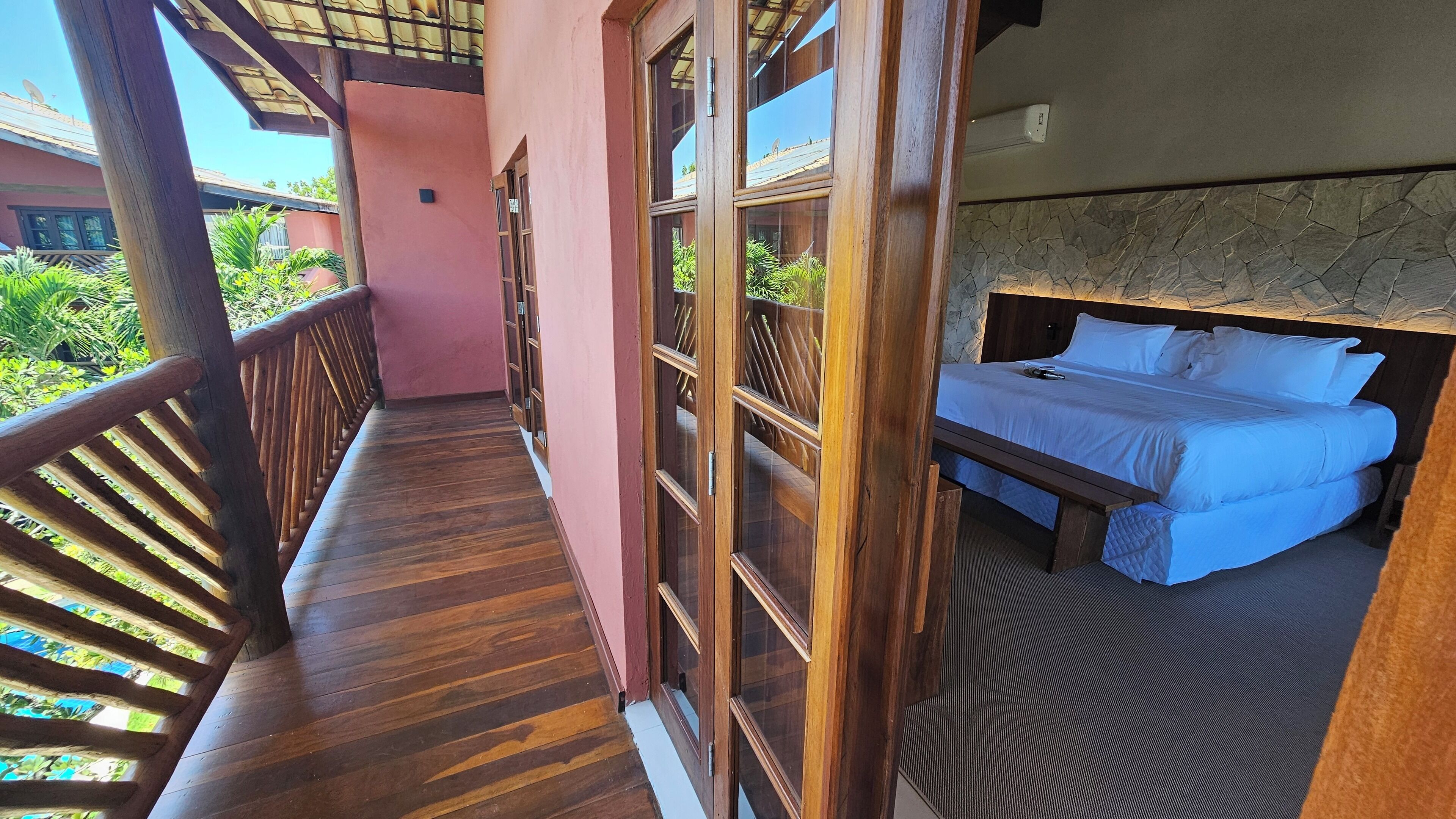 A balcony with wooden railings, a bed with white bedding, and a stone wall.