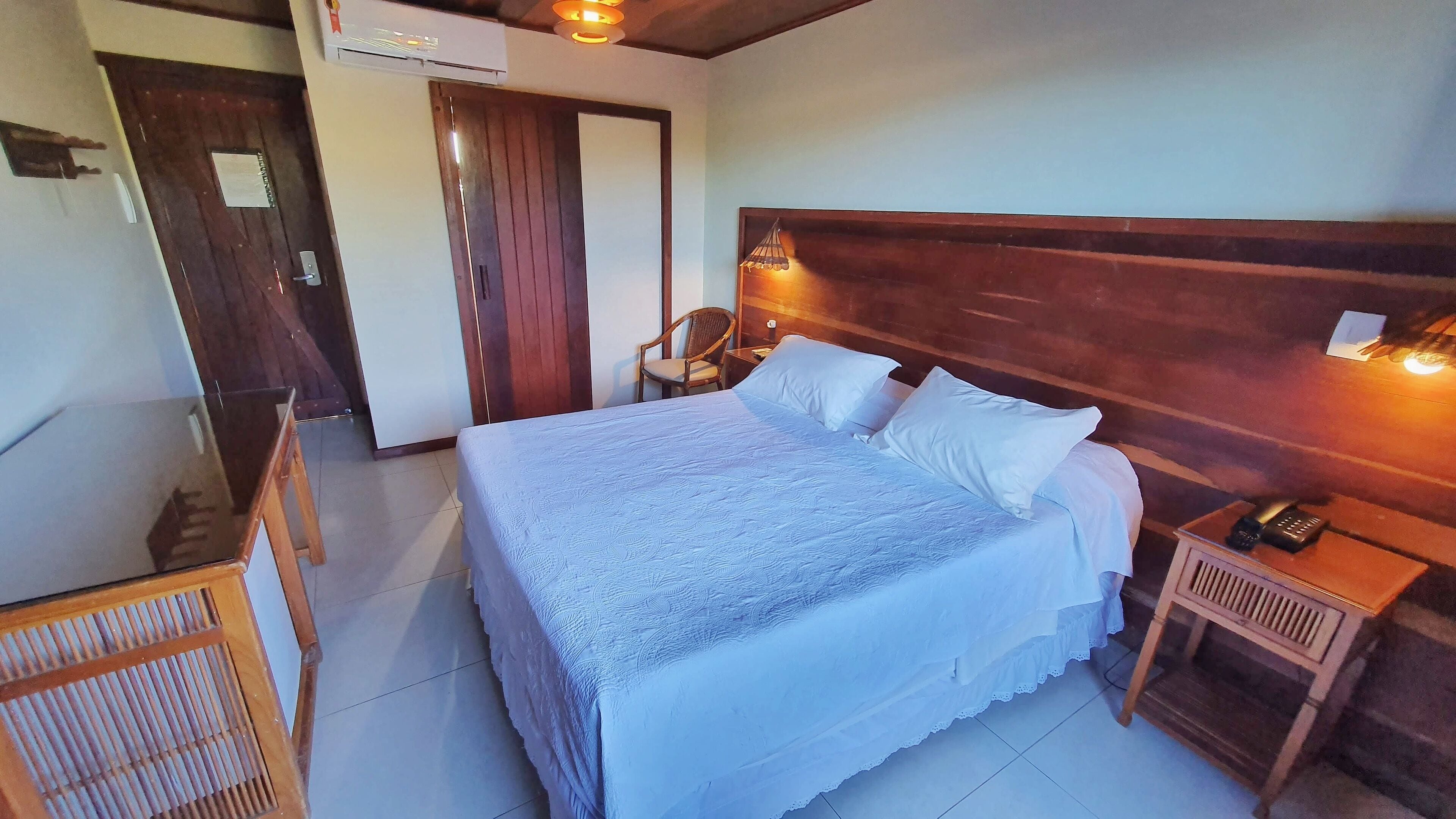 A hotel room with a large bed, a wooden headboard, a bedside table with a lamp, and a chair.