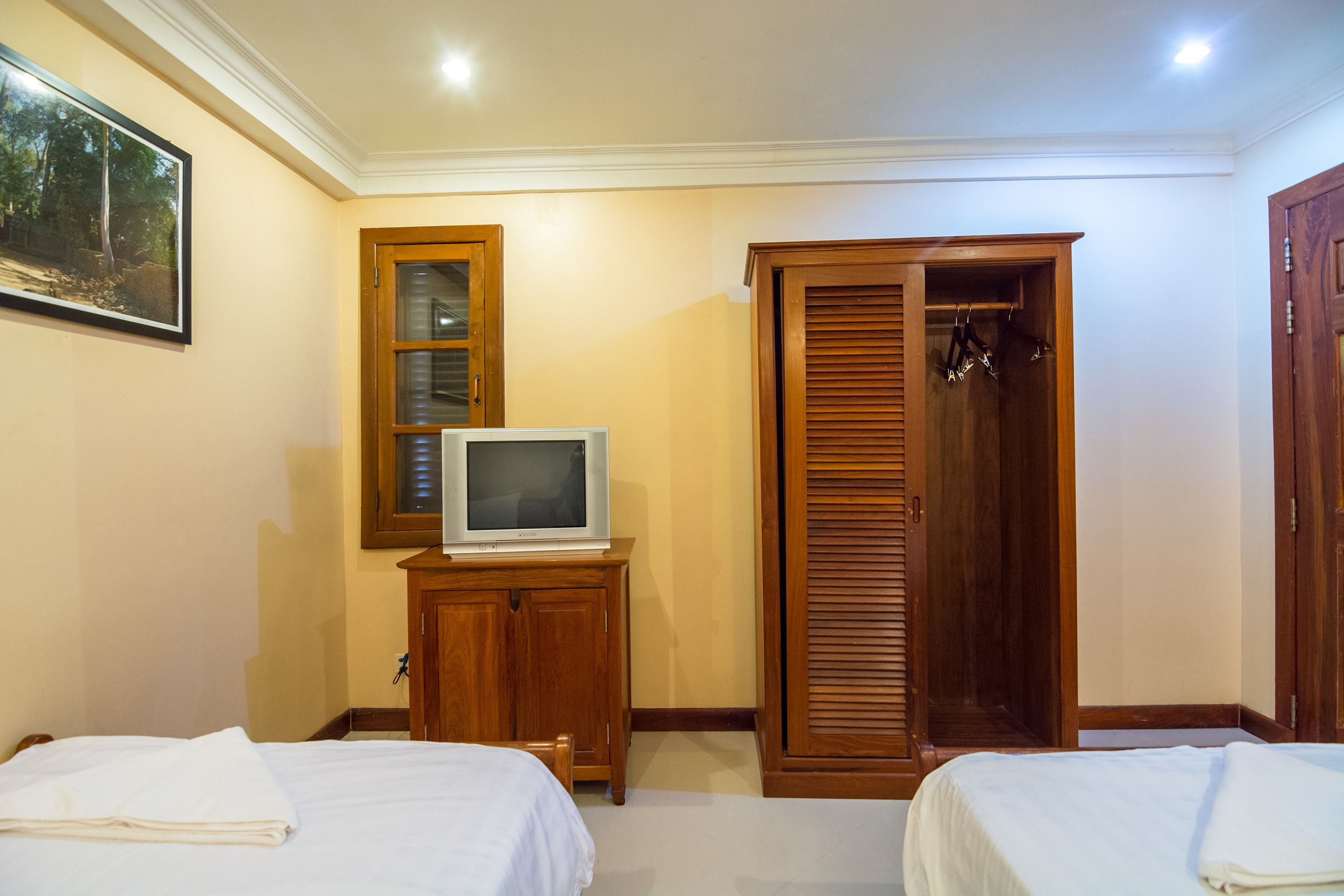 A hotel room with two beds, a wooden wardrobe, a television on a cabinet, and a framed picture on the wall.