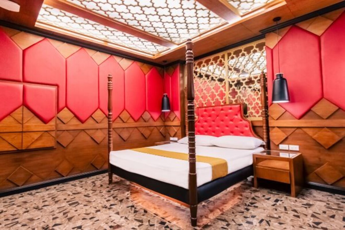 A room with a four-poster bed, a wooden floor, and a patterned ceiling.