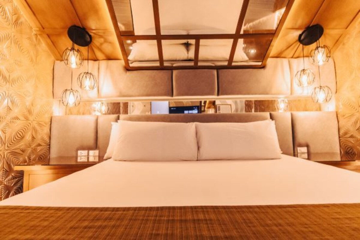 A bedroom with a large bed, headboard with built-in lighting, and a wooden ceiling design.