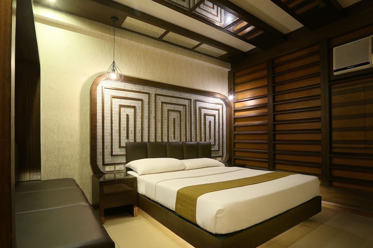 A modern hotel room with a large bed, a nightstand, and a built-in bench.