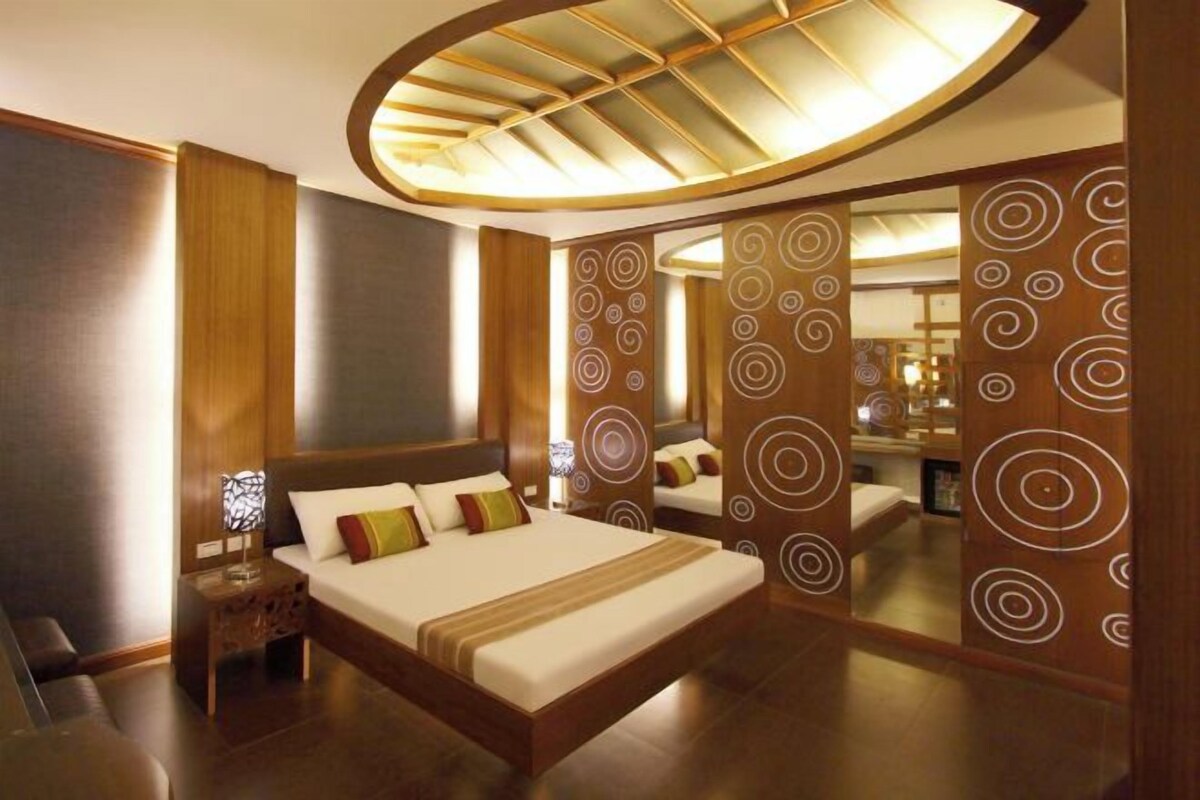 A modern hotel room with a large bed, a wooden headboard, a nightstand, and a mirror with circular patterns.