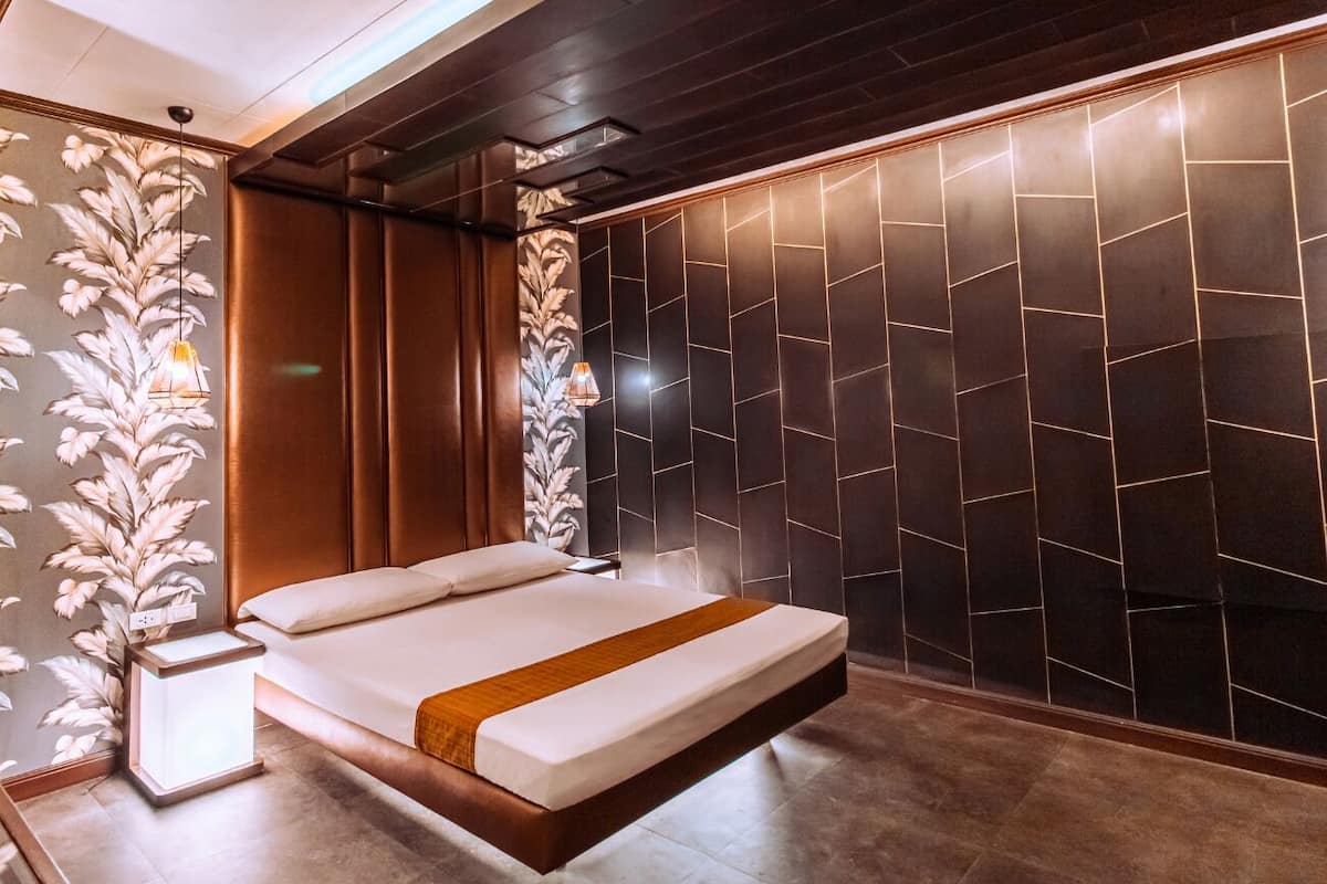A modern bedroom with a large bed, dark wall panels, and a decorative wall panel on the left.