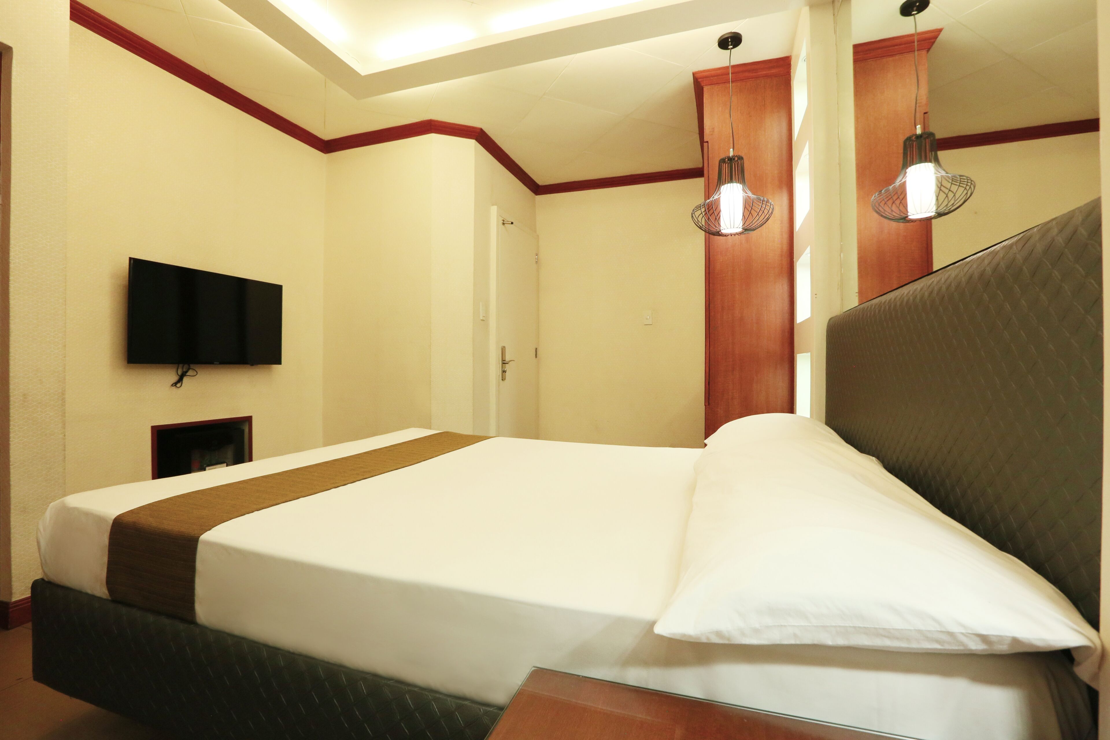 A hotel room with a large bed, a flat-screen TV mounted on the wall, and a wooden door.