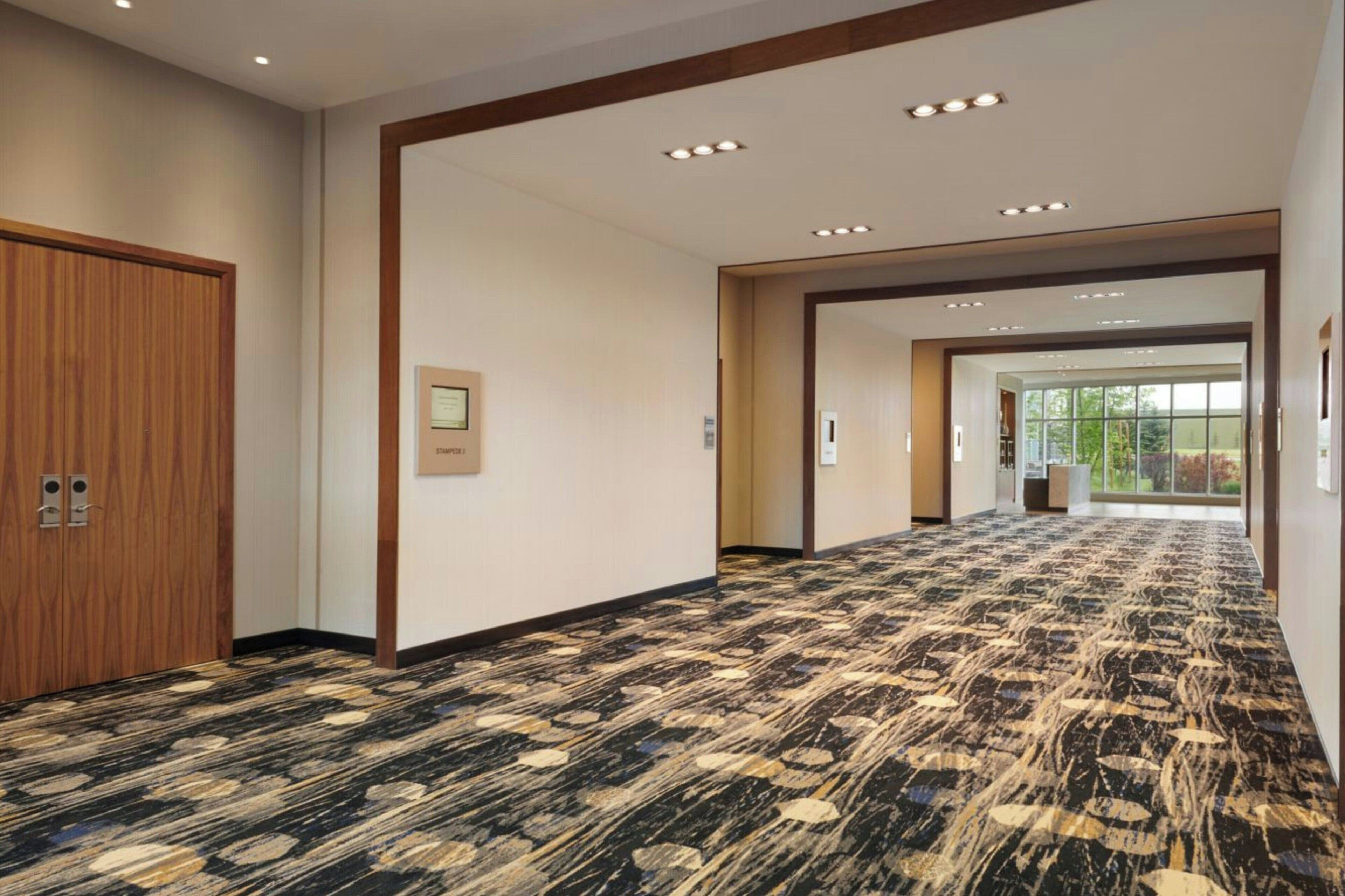 Pasillo de hotel con alfombra estampada, puertas de madera e iluminación empotrada.