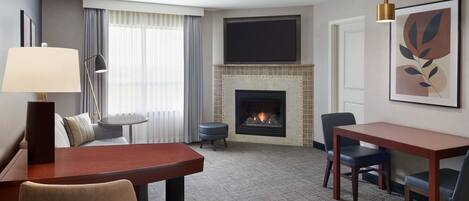 Een hotelkamer met een open haard, een eettafel, een bank en een aan de muur bevestigde televisie.