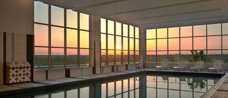 A swimming pool with a sunset view, lounge chairs, and a stack of towels.