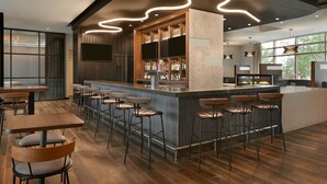A modern bar area with a central counter, multiple bar stools, and a seating area with tables and chairs. - Courtyard by Marriott Calgary Airport (Calgary)