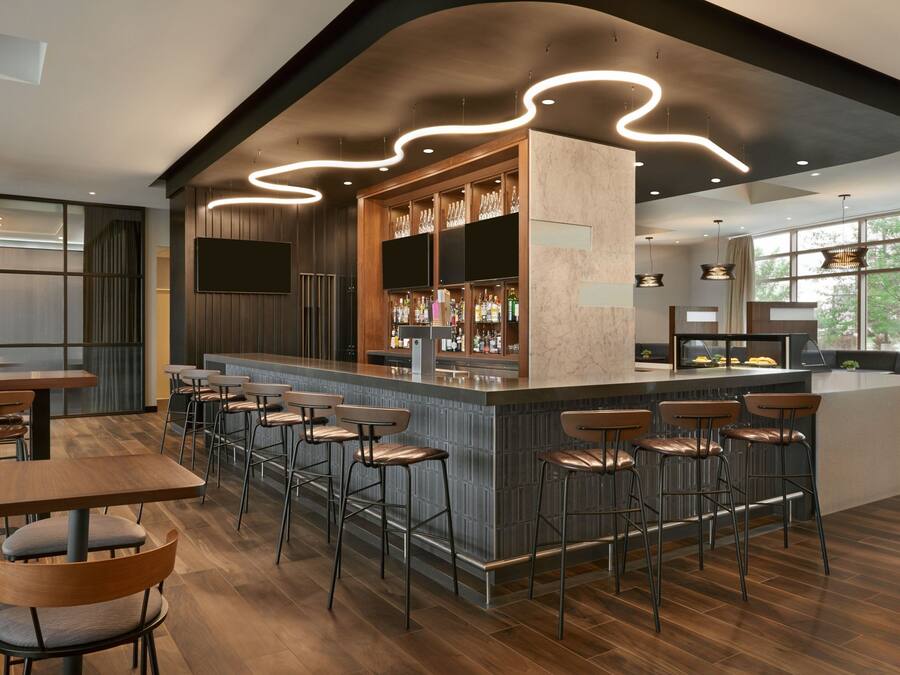 Zona de bar moderna con barra central, varios taburetes y un área de estar con mesas y sillas.