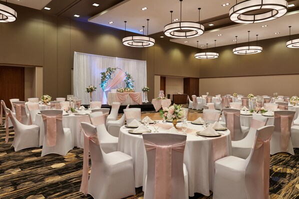 A banquet hall with round tables, white chairs, and pink sashes.