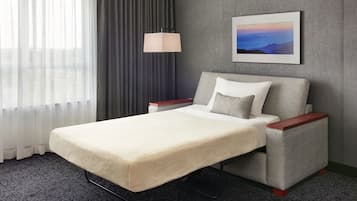 Habitación de hotel con cama, mesita de noche, lámpara, un cuadro y vistas al exterior a través de la ventana.