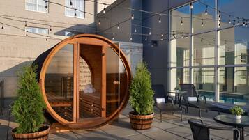 A circular wooden structure with a glass door, two potted plants, and a seating area with a table and chairs.