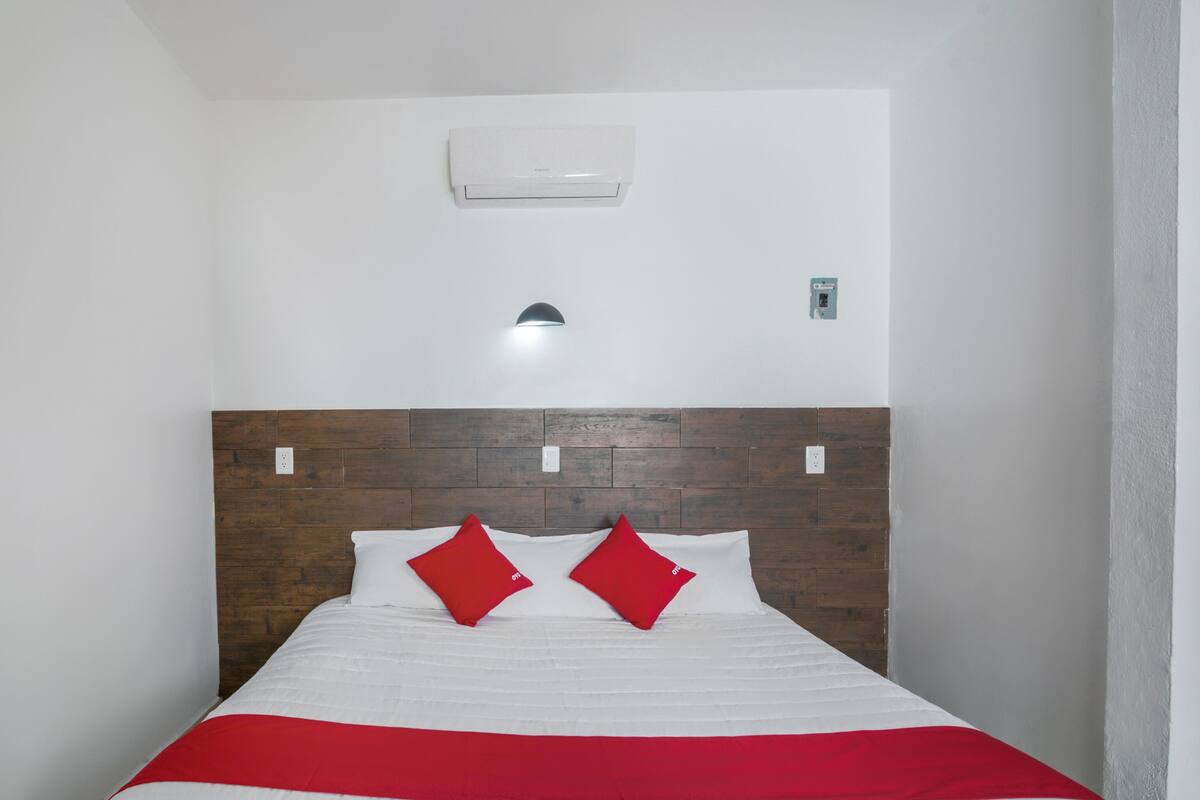 A hotel room with a wooden headboard, white bedding, and a red accent pillow.
