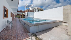 Una piscina con bordo piastrellato, una zona coperta con tetto e una panchina.