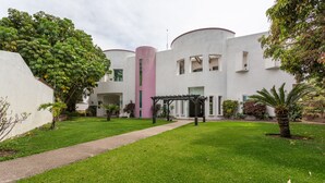 Un cortile con un vialetto che conduce a un edificio con una colonna rosa, circondato da vegetazione e un pergolato.