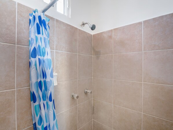 Ducha con azulejos color beige, cortina de baño azul y cabezal de ducha de mano.