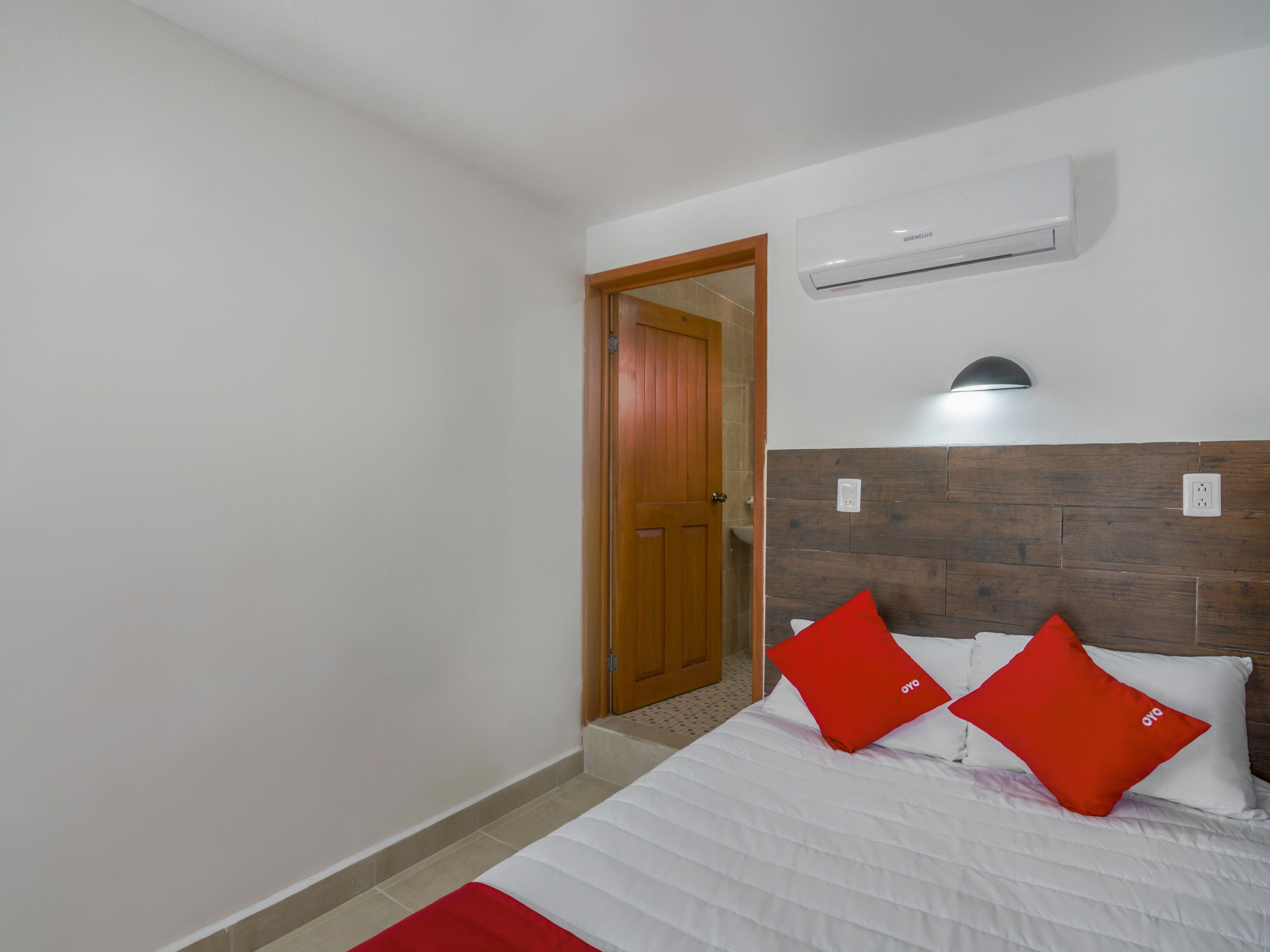 A bedroom with a bed, a wooden door, an air conditioning unit, and a wall-mounted light fixture.