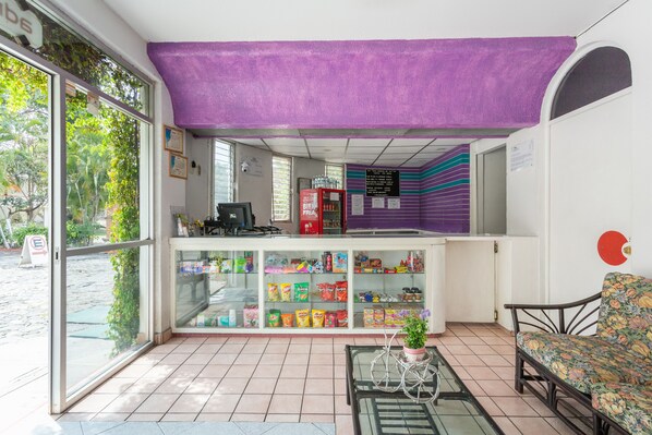 Una habitación con un expositor de vidrio lleno de bocadillos, un toldo morado y una zona de estar con un sofá floral.