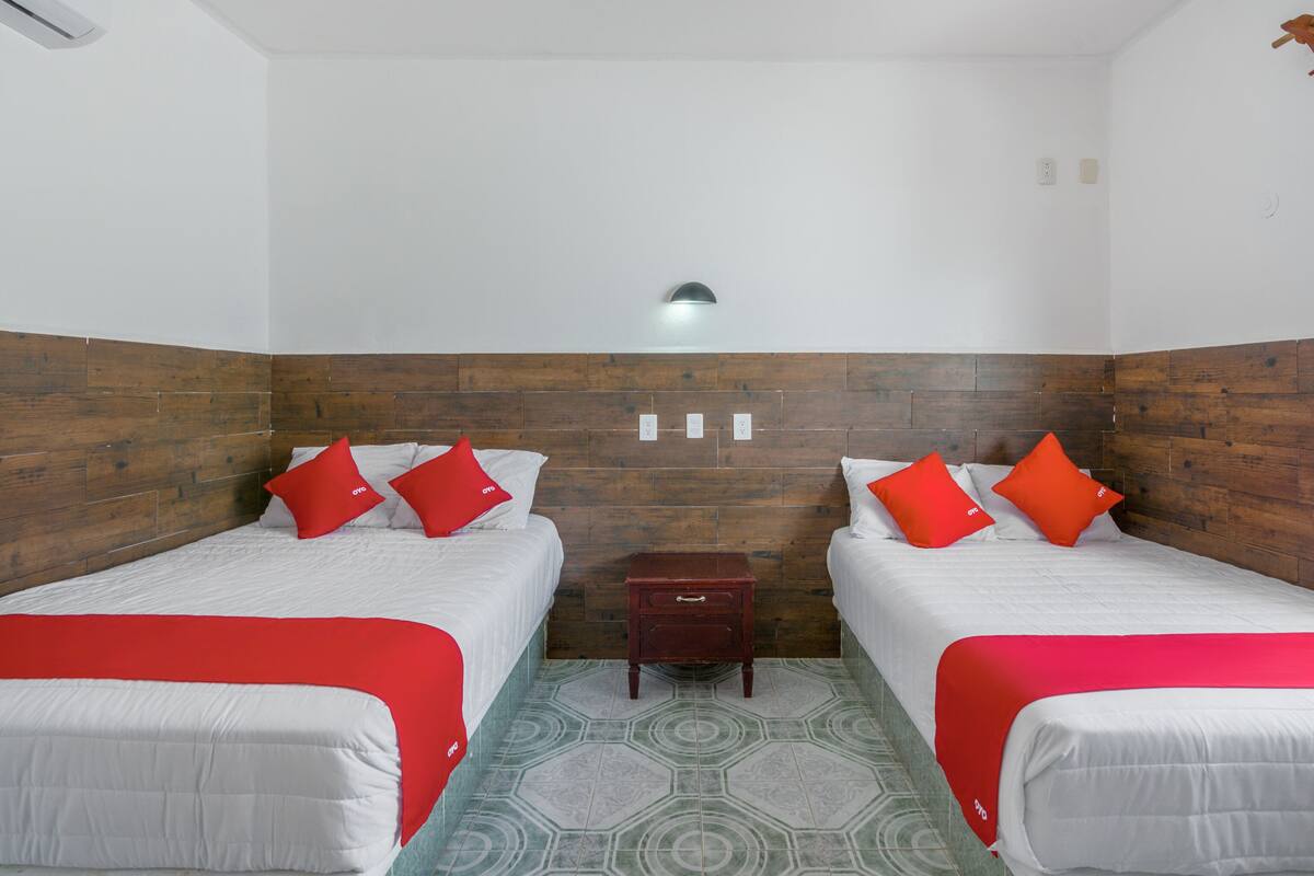 A hotel room with two beds, each with red and white bedding, a wooden headboard, a small wooden nightstand, and a patterned floor.