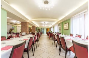 A hotel dining area with tables set for service, a brick column, and framed artwork on the walls. - Hotel Santa Maria (Baunei)