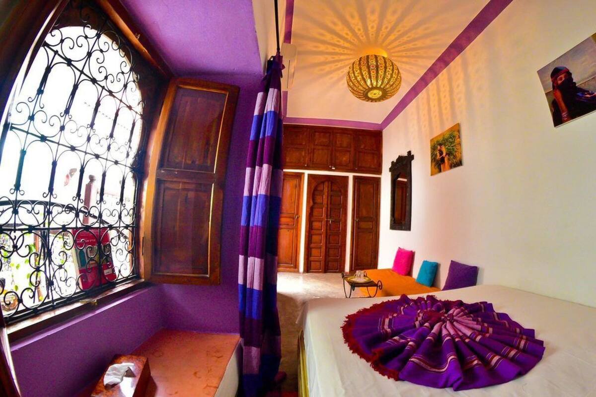 A bedroom with a large bed, a window with decorative iron bars, a ceiling fan, and a wooden wardrobe.