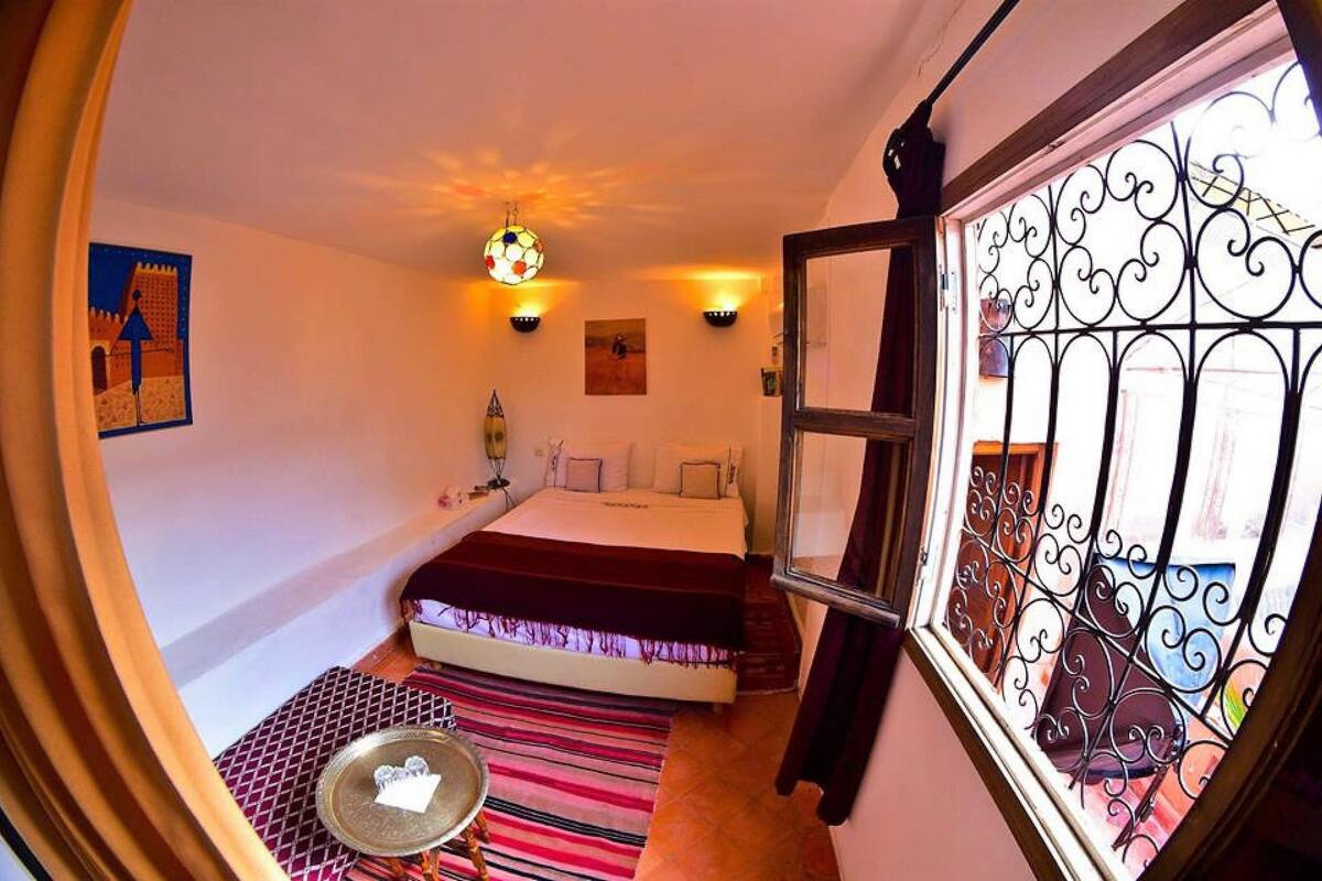 A bedroom with a bed, a window with decorative iron bars, a colorful striped rug, and a small table with a tray.