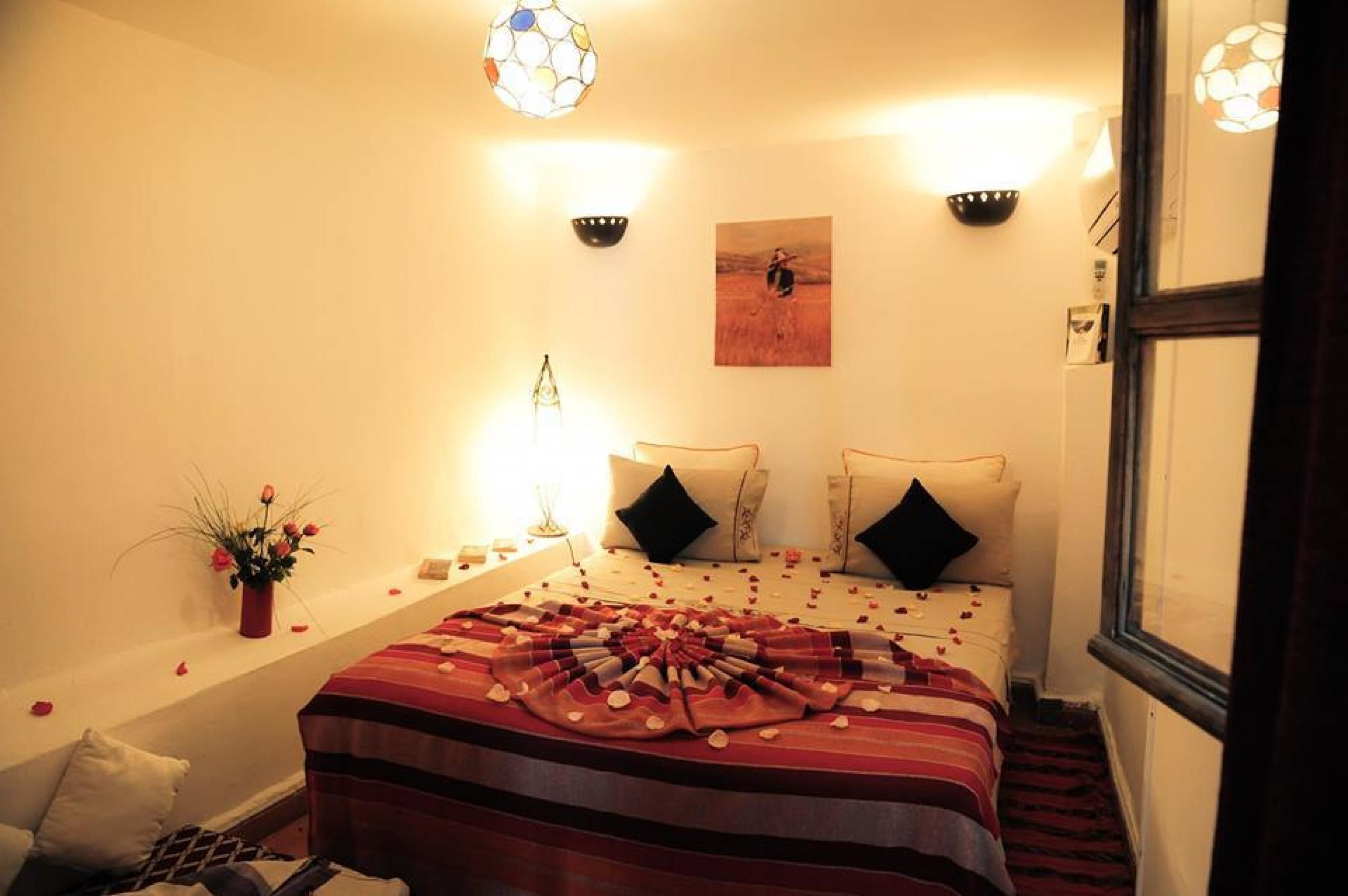 A hotel room with a bed, two wall sconces, a painting, and a vase with flowers.