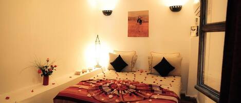 A hotel room with a bed, two wall sconces, a painting, and a vase with flowers.
