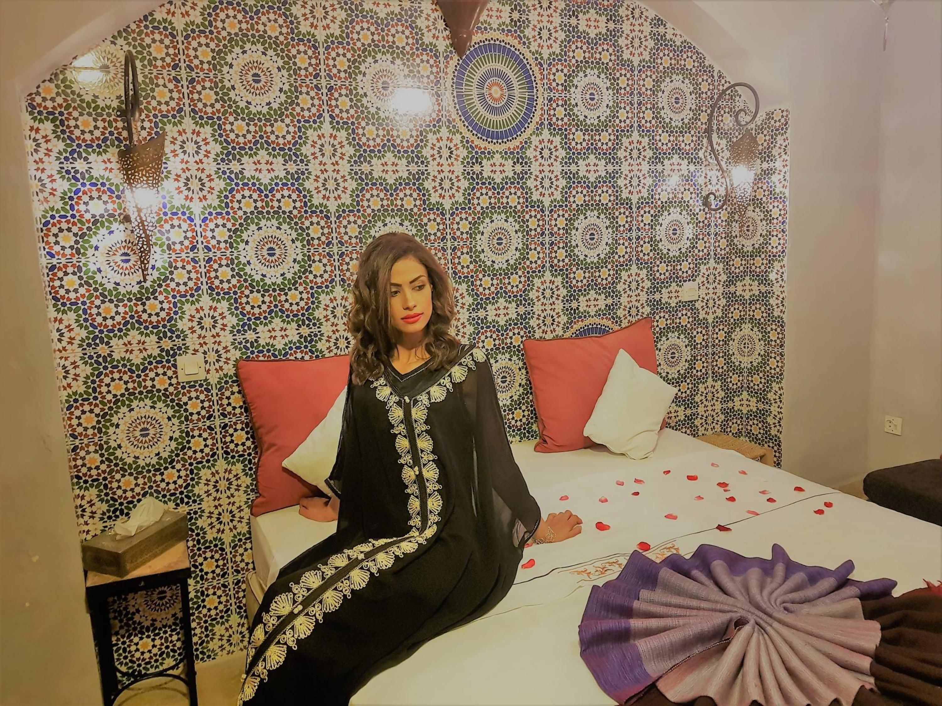 A room with a patterned wall, a bed with red and white pillows, and a purple decorative item on the bed.