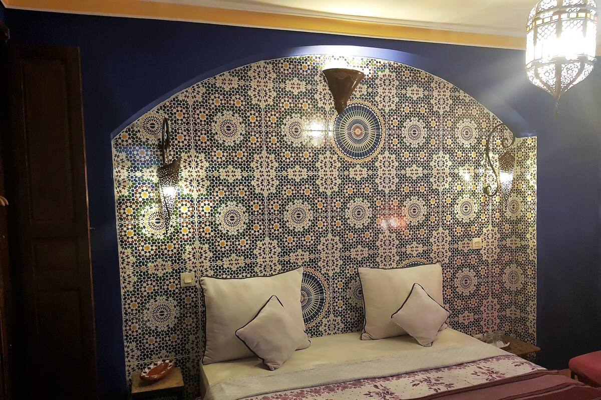 A room with a patterned tile wall, a bed with a floral bedspread, and a hanging light fixture.