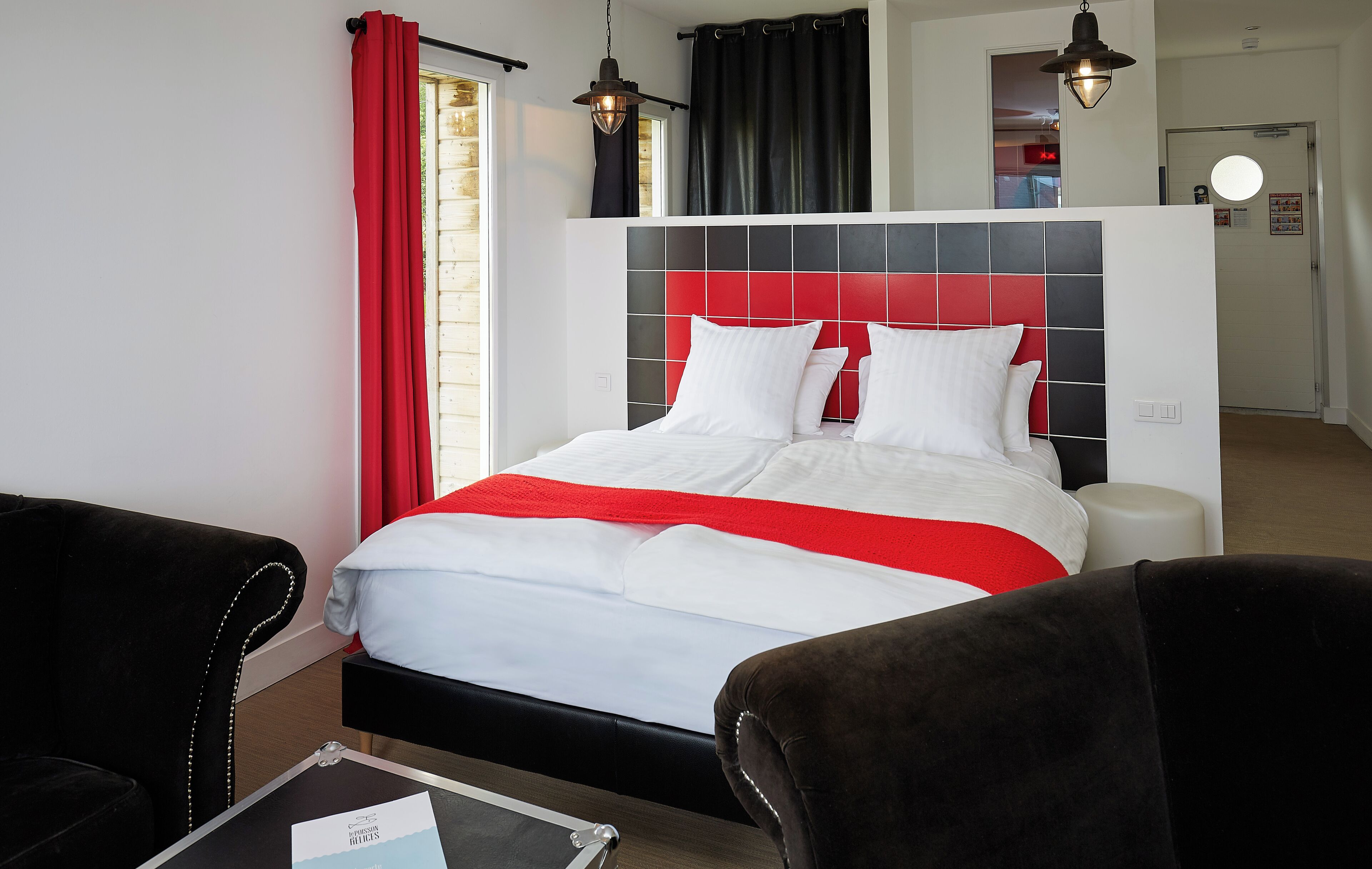 A hotel room with a bed, two chairs, a table, and a window with curtains.