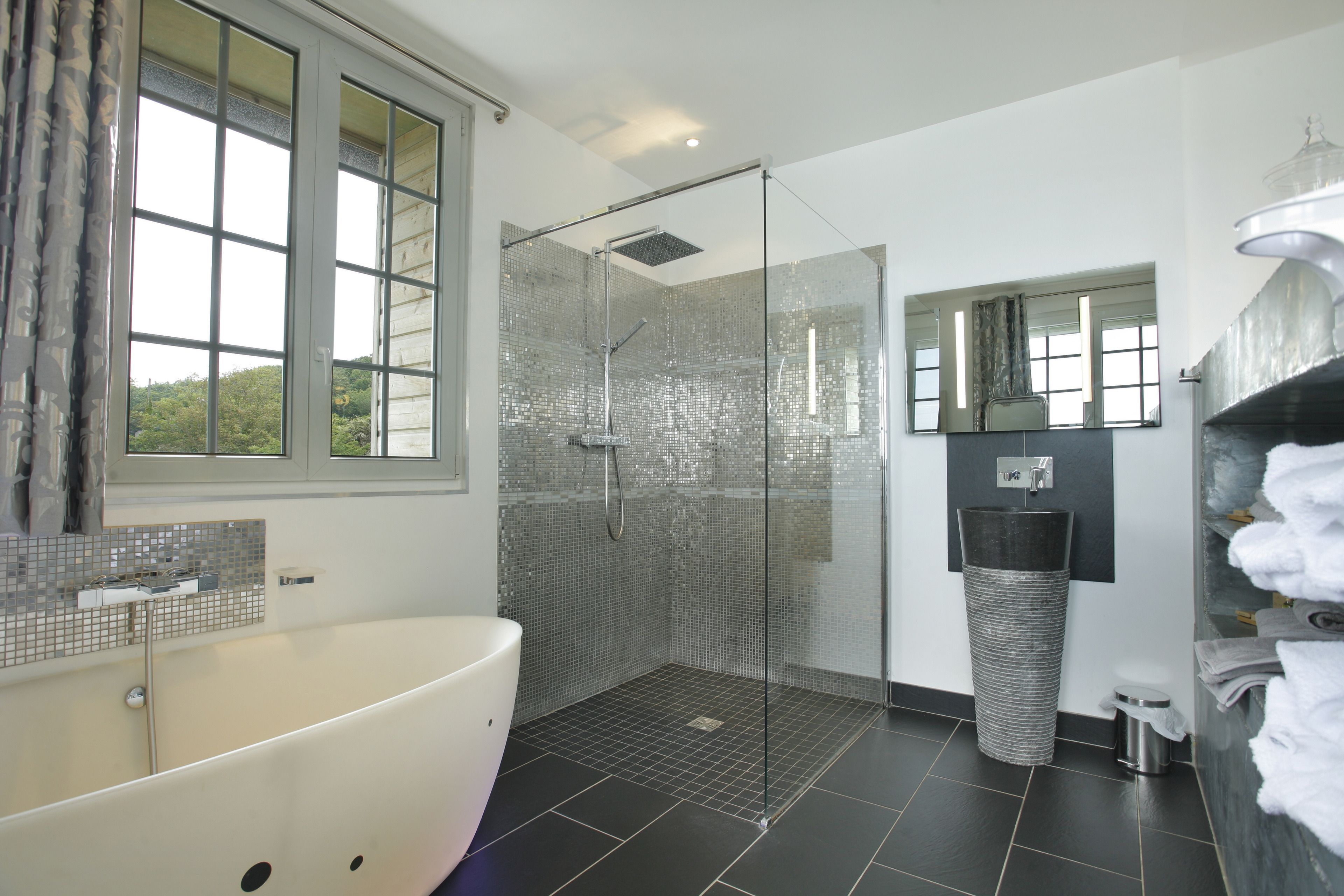 A modern bathroom with a large bathtub, a glass-enclosed shower, and a sink with a mirror above it.