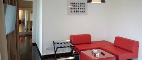 Una habitación de hotel moderna con un sofá rojo, una mesita, un televisor y una lámpara fijada a la pared.