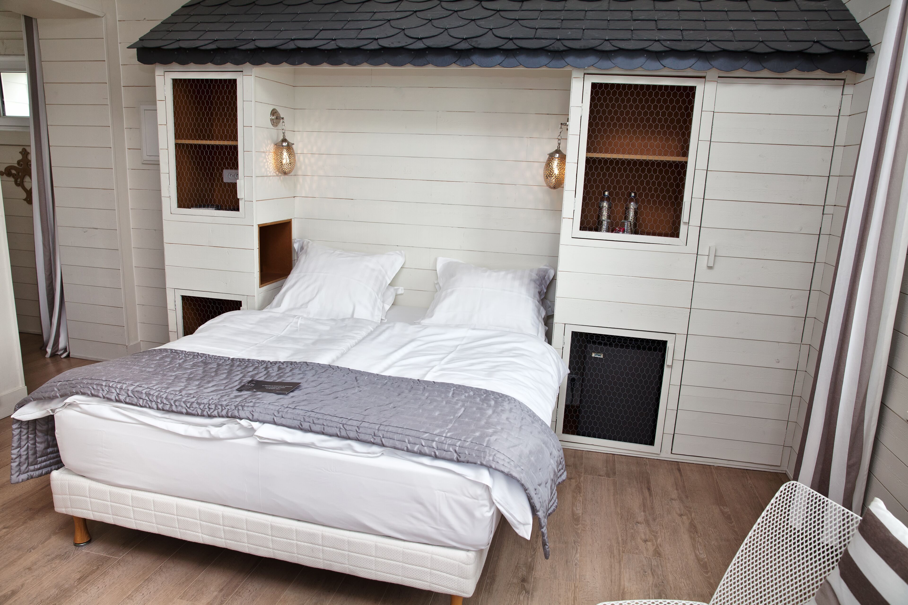 A bedroom with a bed, two nightstands, a window with a mesh screen, and a ceiling with a dark tile roof.