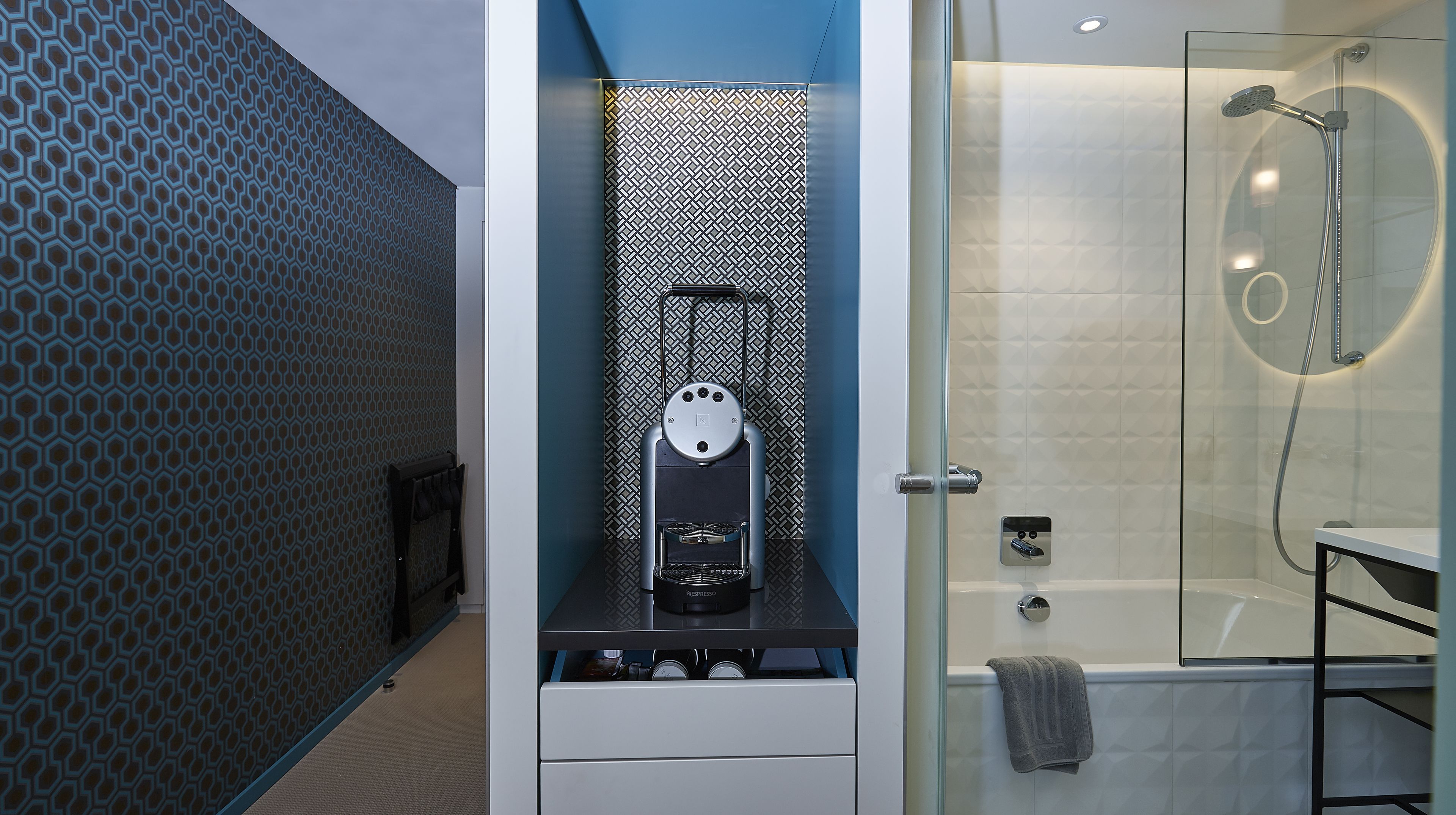 A modern bathroom with a shower, a Nespresso coffee machine, and a patterned wall.