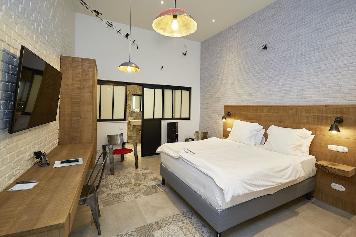 Una habitación de hotel moderna con una cama grande, un escritorio, una silla, un televisor y un diseño de pared único.