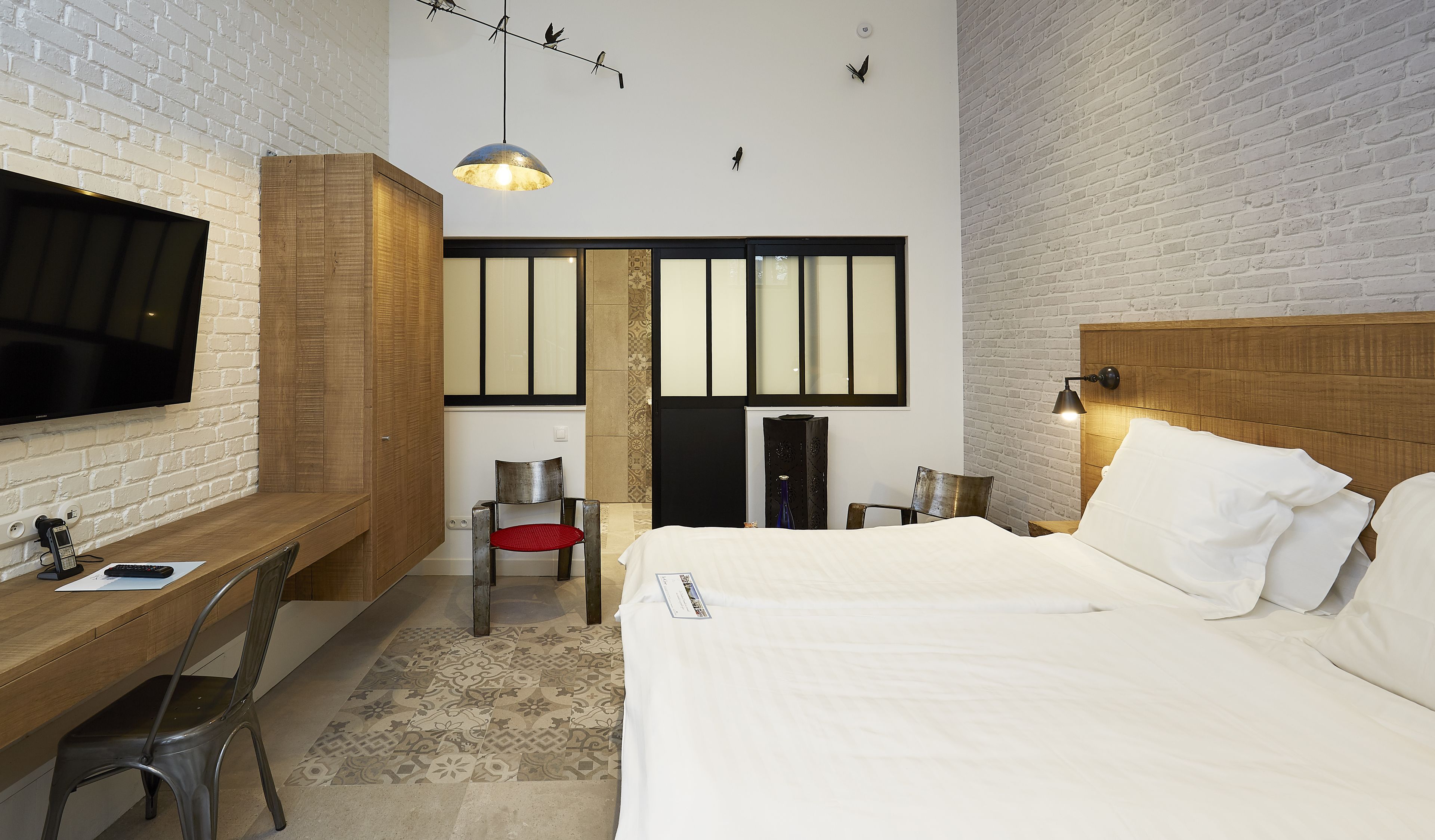 A hotel room with a bed, a desk with a chair, a TV, and a large window.