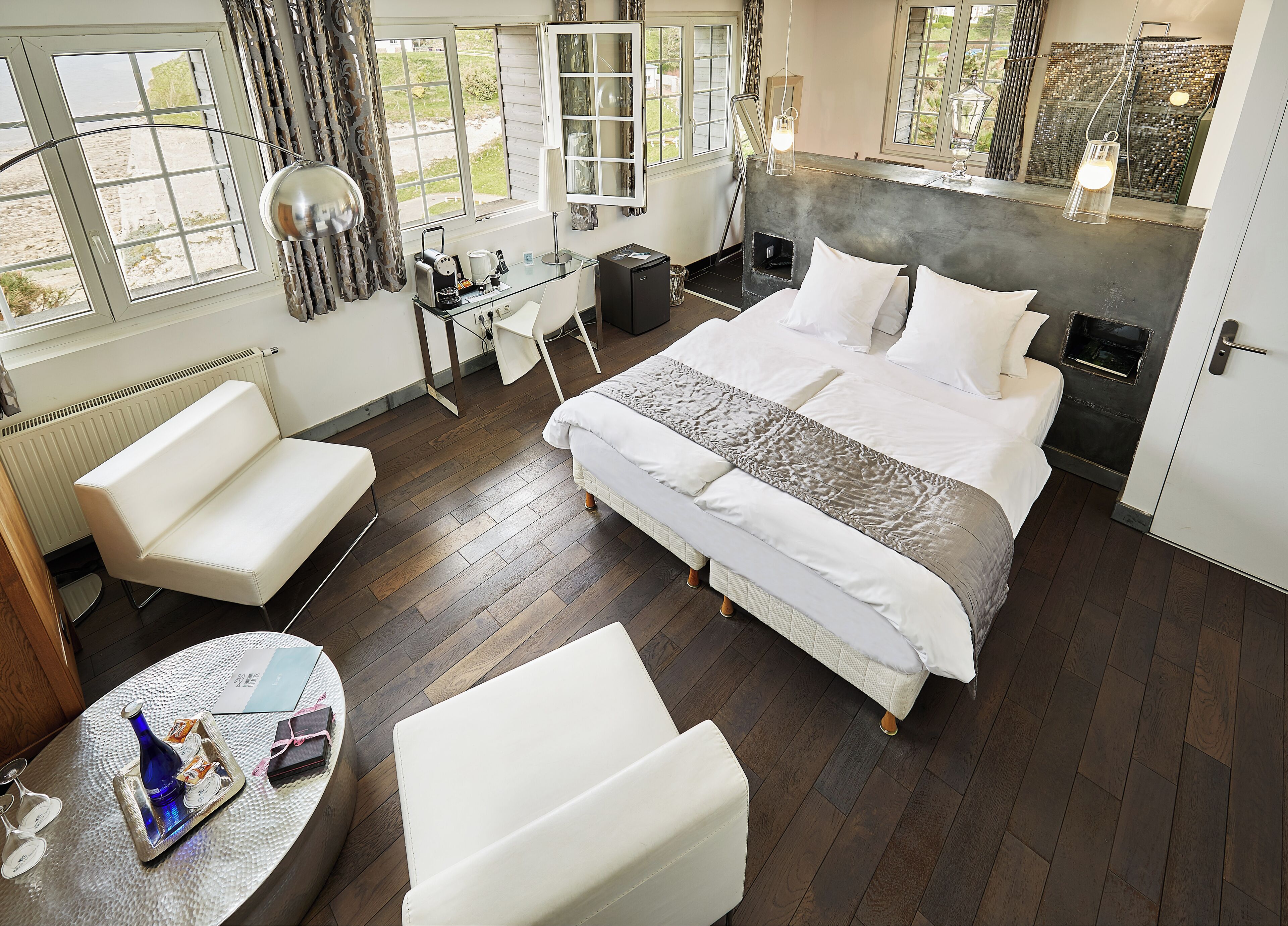 Habitación de hotel moderna con una cama grande, un área de descanso, un escritorio con computadora y vista al exterior.