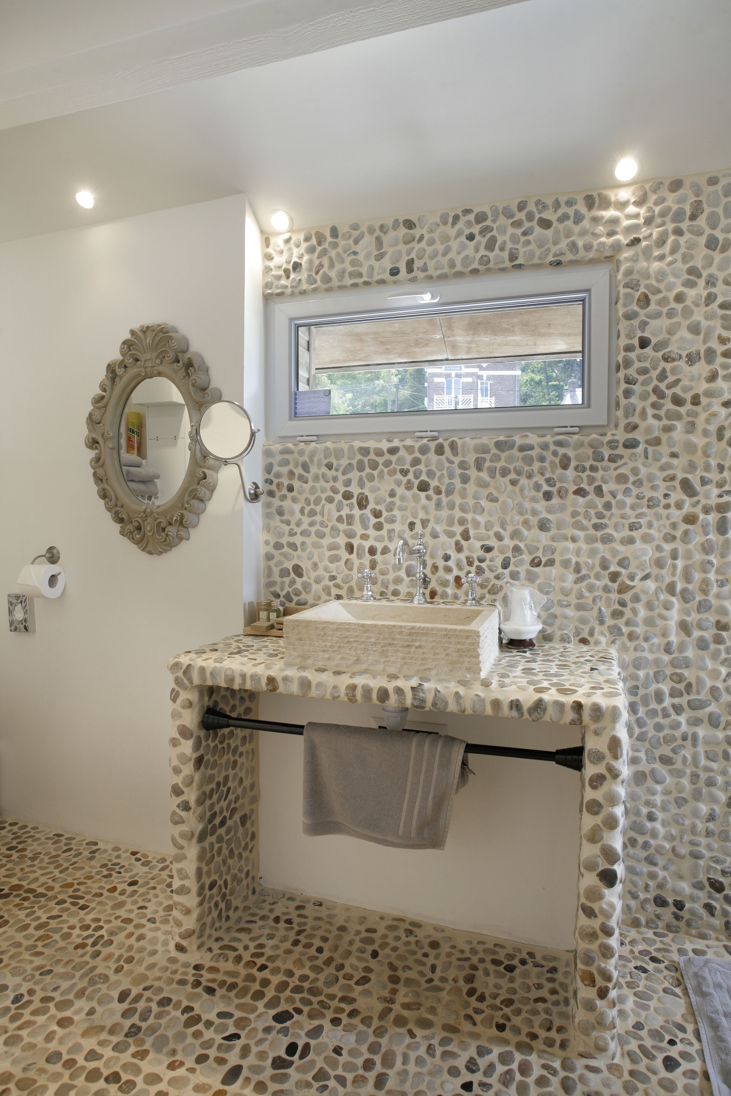 A bathroom with a stone mosaic wall, a sink with a mirror above it, and a window above the mirror.