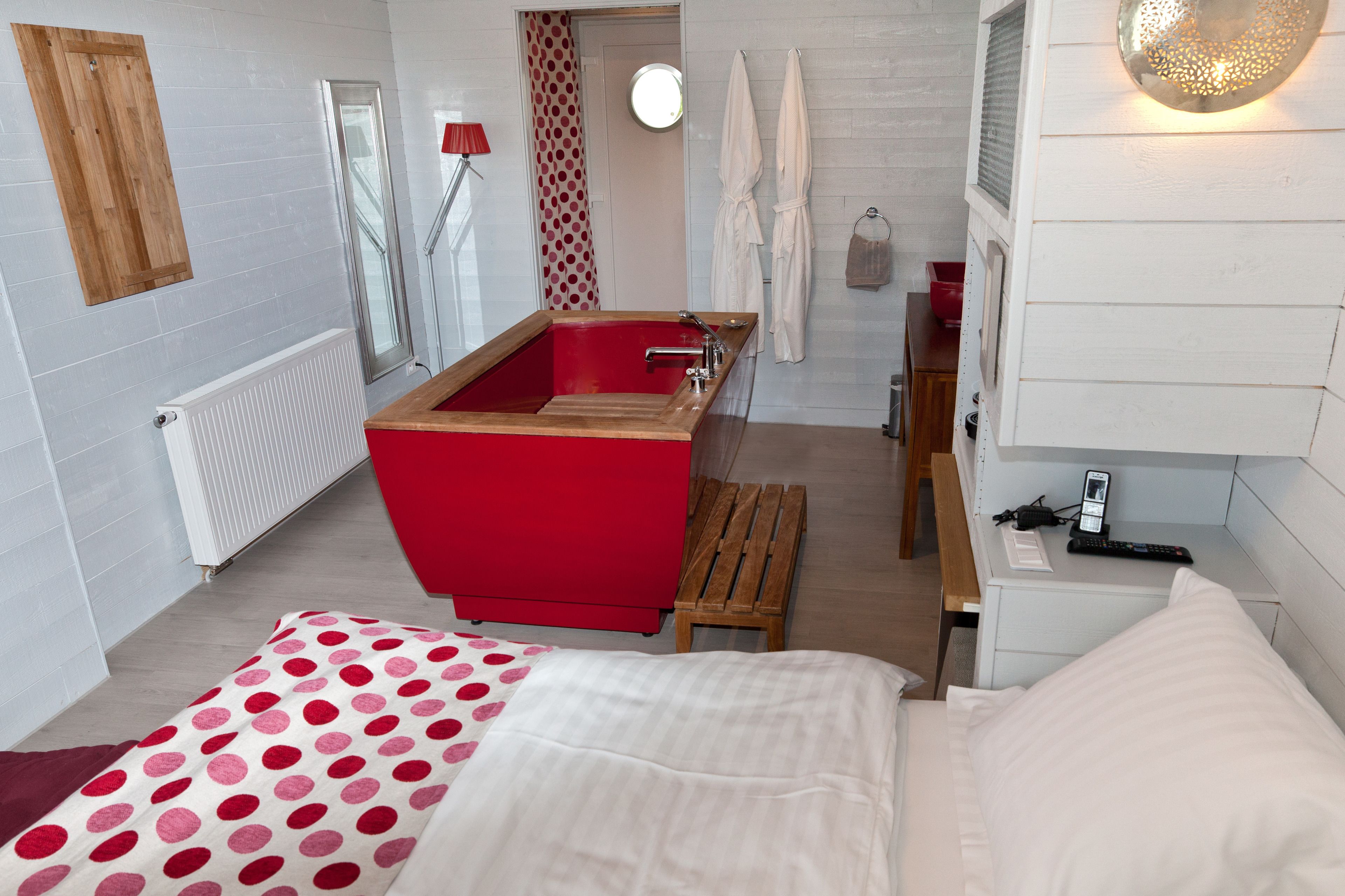 Un baño moderno con una bañera roja, un banco de madera y una mesita con un teléfono y un control remoto.