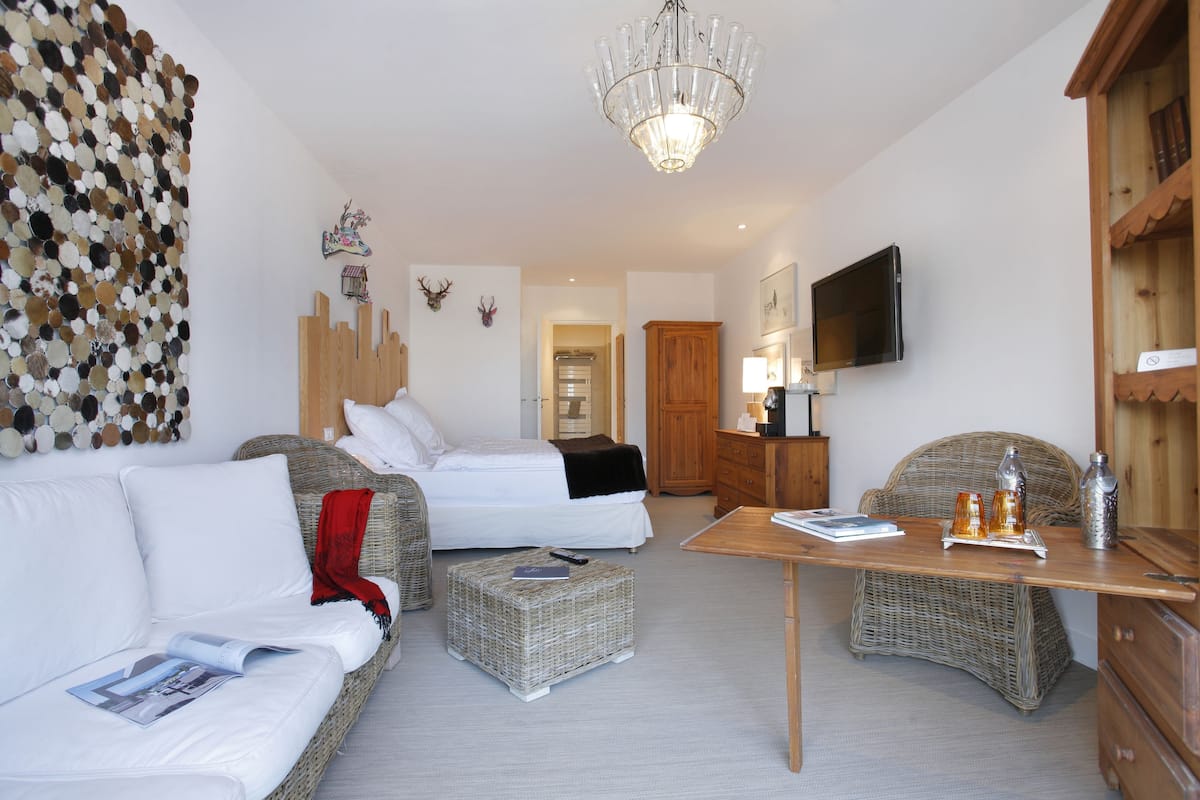 Habitación de hotel con dos camas, una mesa de comedor, muebles de mimbre, un candelabro y un televisor.
