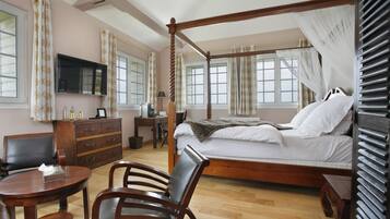 A four-poster bed with a canopy, a television mounted on the wall, a desk with a chair, and a small round table with a chair.