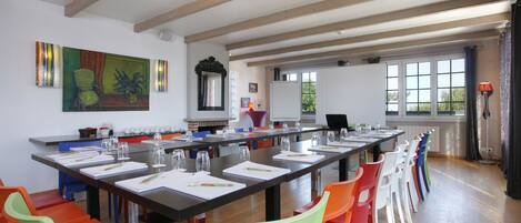 A conference room with a long table, colorful chairs, and a large painting on the wall.